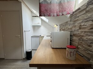 Une cuisine de taille réduite, dotée d’un plan de travail en bois, d’un réfrigérateur blanc et d’une poubelle.