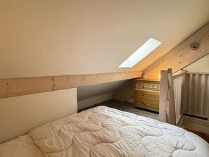 A bedroom with a sloped ceiling, a skylight, a bed, a dresser, and a wooden staircase. - ROYAL19 (Cauterets)