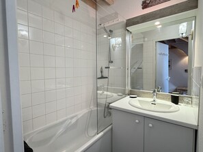 Une salle de bain moderne avec des carreaux blancs, une douche en verre, un meuble-lavabo et un grand miroir.