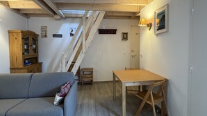 Ein gemütliches Zimmer mit Holzbalkendecke, einer Couch, einem Esstisch und einer Treppe.