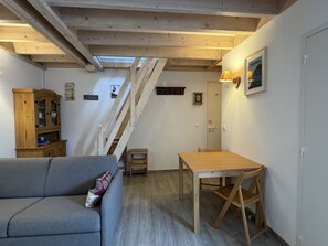 A cozy room with a wooden ceiling, a sofa, a dining table, and a staircase.