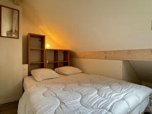 Un lit simple avec une couette blanche, une tête de lit en bois et une table de chevet avec une lampe.
