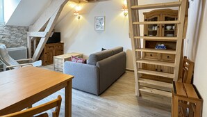 Ein Loft-Zimmer mit Holztisch, grauem Sofa und einer Holzleiter.