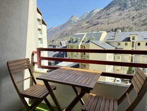 A balcony with wooden furniture, a view of buildings and mountains in the background.