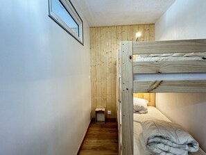 Une petite pièce étroite avec un lit superposé, des murs en bois et une petite fenêtre.
