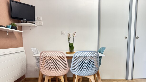 A dining area with two chairs, a table, a potted plant, and a television mounted on a shelf. - Joli 3 pièces 40m2. 2 chambres (Cauterets)