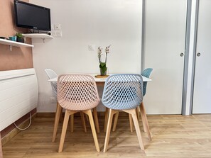 A dining area with two chairs, a table, a potted plant, and a television mounted on a shelf.