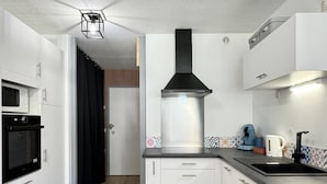 A compact kitchen with white cabinets, a black range hood, a microwave, and a kettle. - Joli 3 pièces 40m2. 2 chambres (Cauterets)