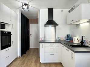 A compact kitchen with white cabinets, a black range hood, a microwave, and a kettle. - Joli 3 pièces 40m2. 2 chambres (Cauterets)