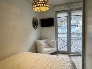 Un dormitorio con una cama, una silla, un televisor y una ventana con vista a edificios.