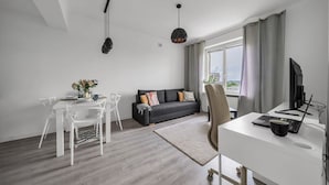 A modern living room with a sofa, dining table, and a desk with a computer. - Śródmieście Apartment - 8th Floor, Workspace, Tram - by Rentujemy (Warszawa)