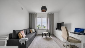 A modern living room with a grey sofa, a small table, a white desk with a laptop, and a TV. - Śródmieście Apartment - 8th Floor, Workspace, Tram - by Rentujemy (Warszawa)