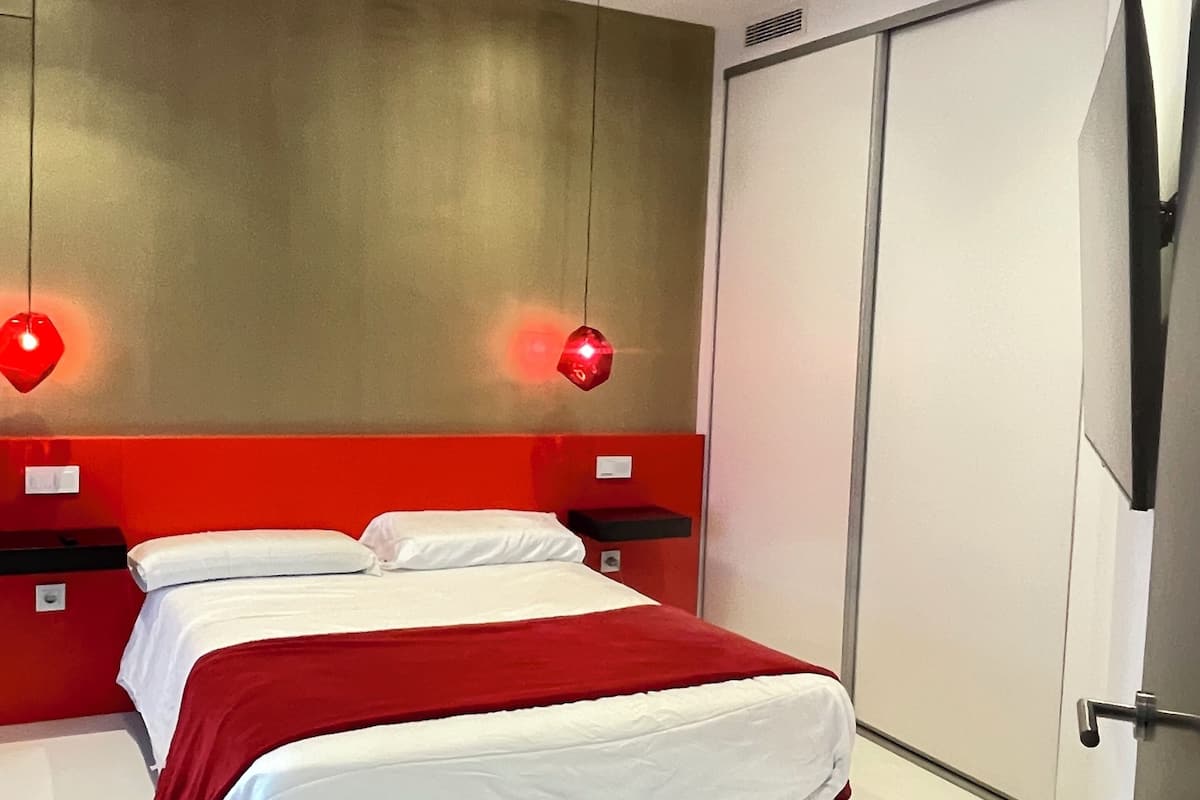 A modern bedroom with a bed, two bedside tables, a wardrobe, and two pendant lights.