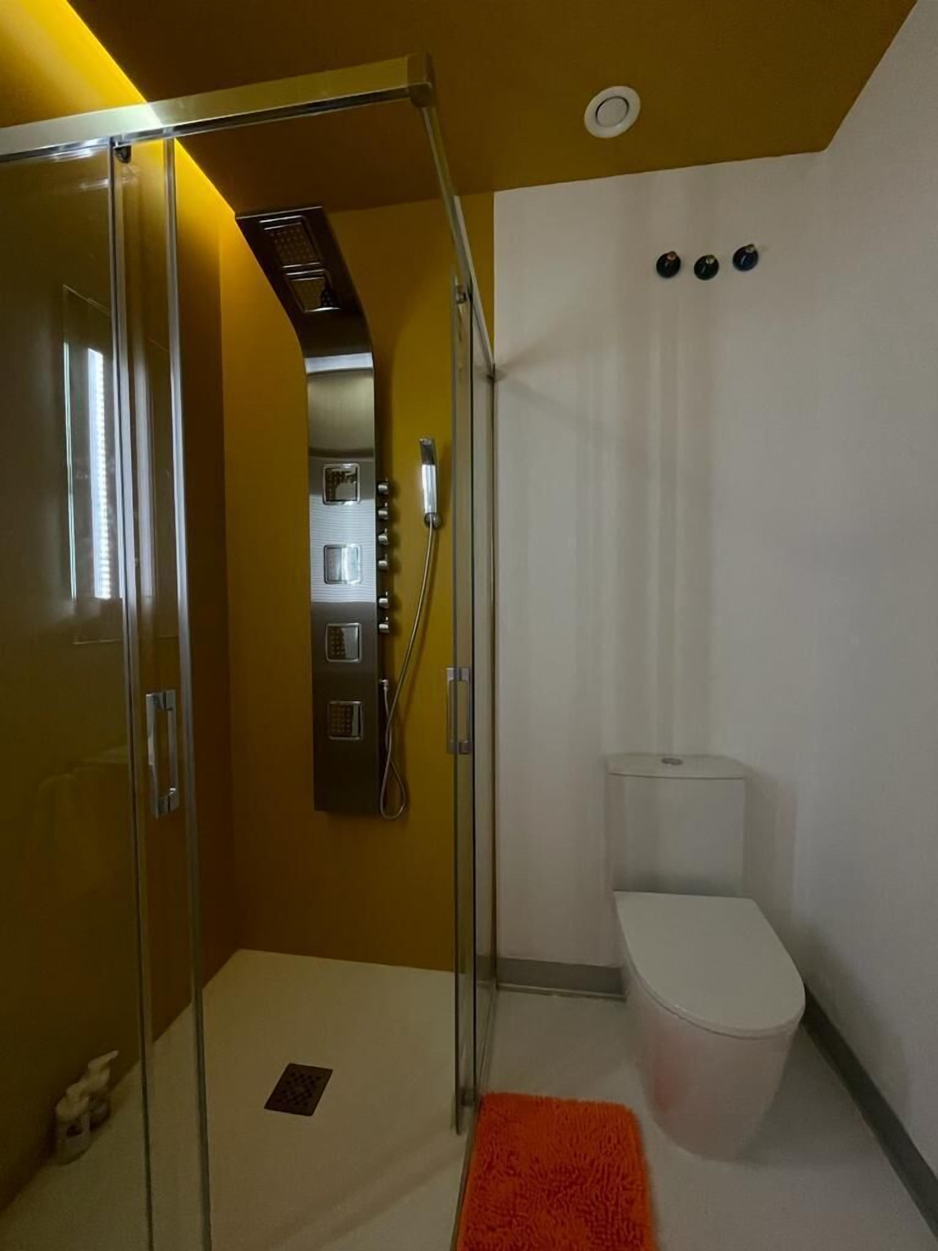 A modern bathroom with a glass shower enclosure, a toilet, and a small rug.