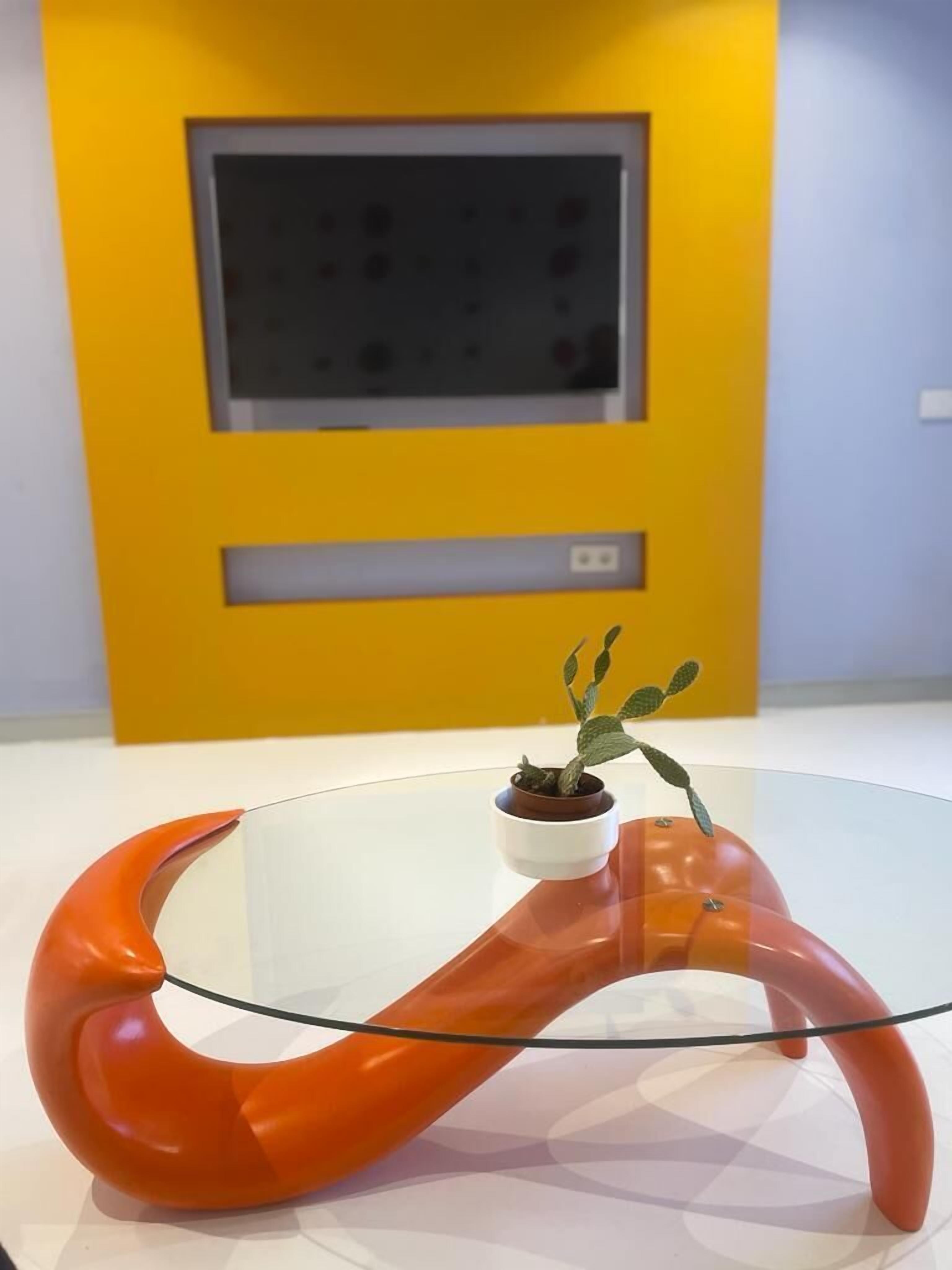 Ein moderner Tisch mit Glasplatte und einem auffälligen orangefarbenen Design.