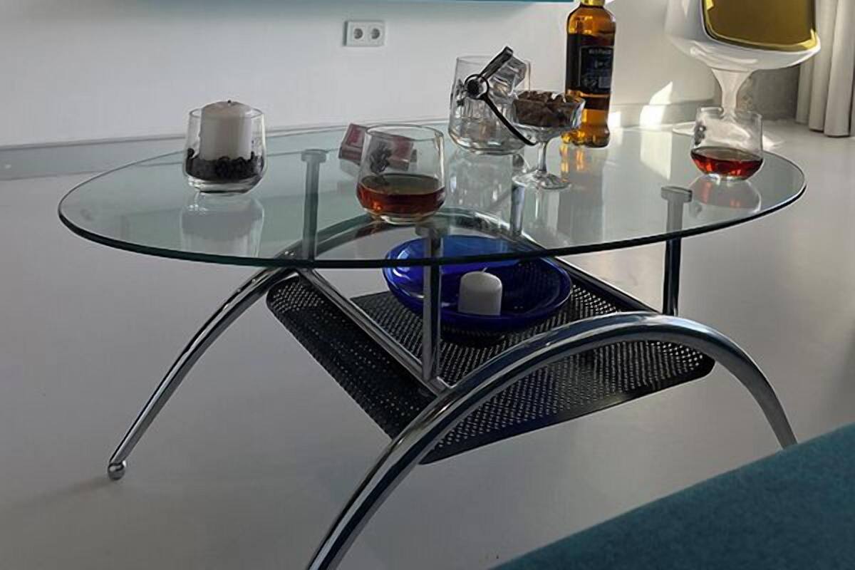 A modern living room with a glass table, a TV mounted on the wall, and a blue shelf below.