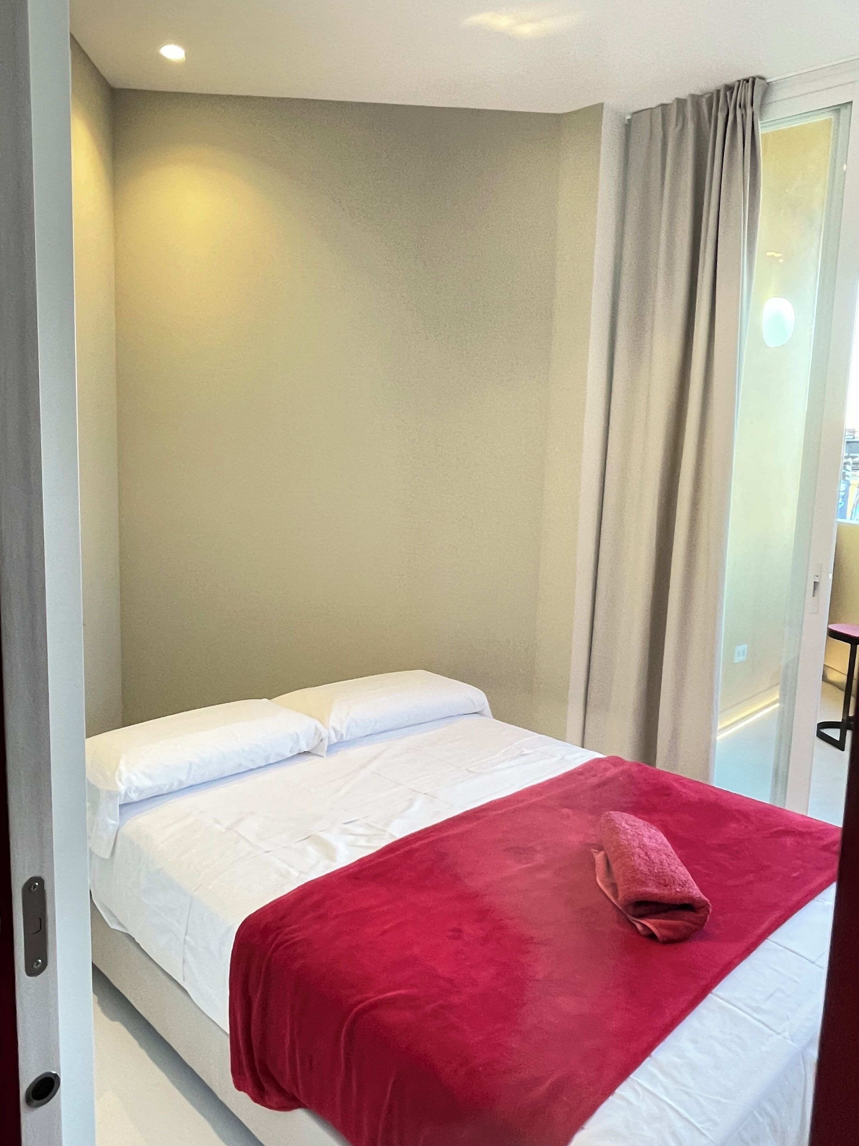 Een hotelkamer met een bed, een rode deken en een raam met gordijnen.
