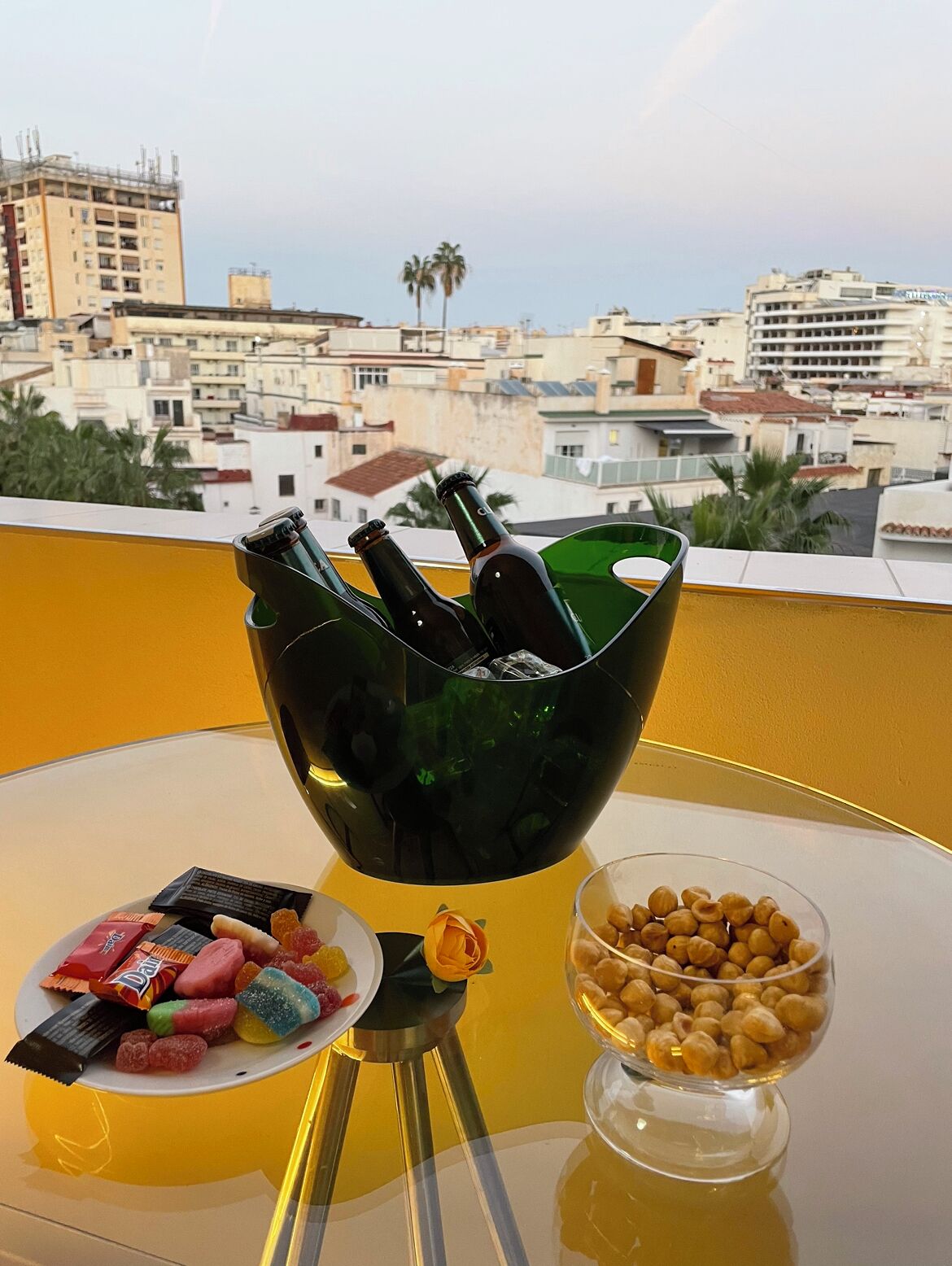 A table with a green glass bowl containing bottles, a plate with assorted candies, and a bowl of peanuts.