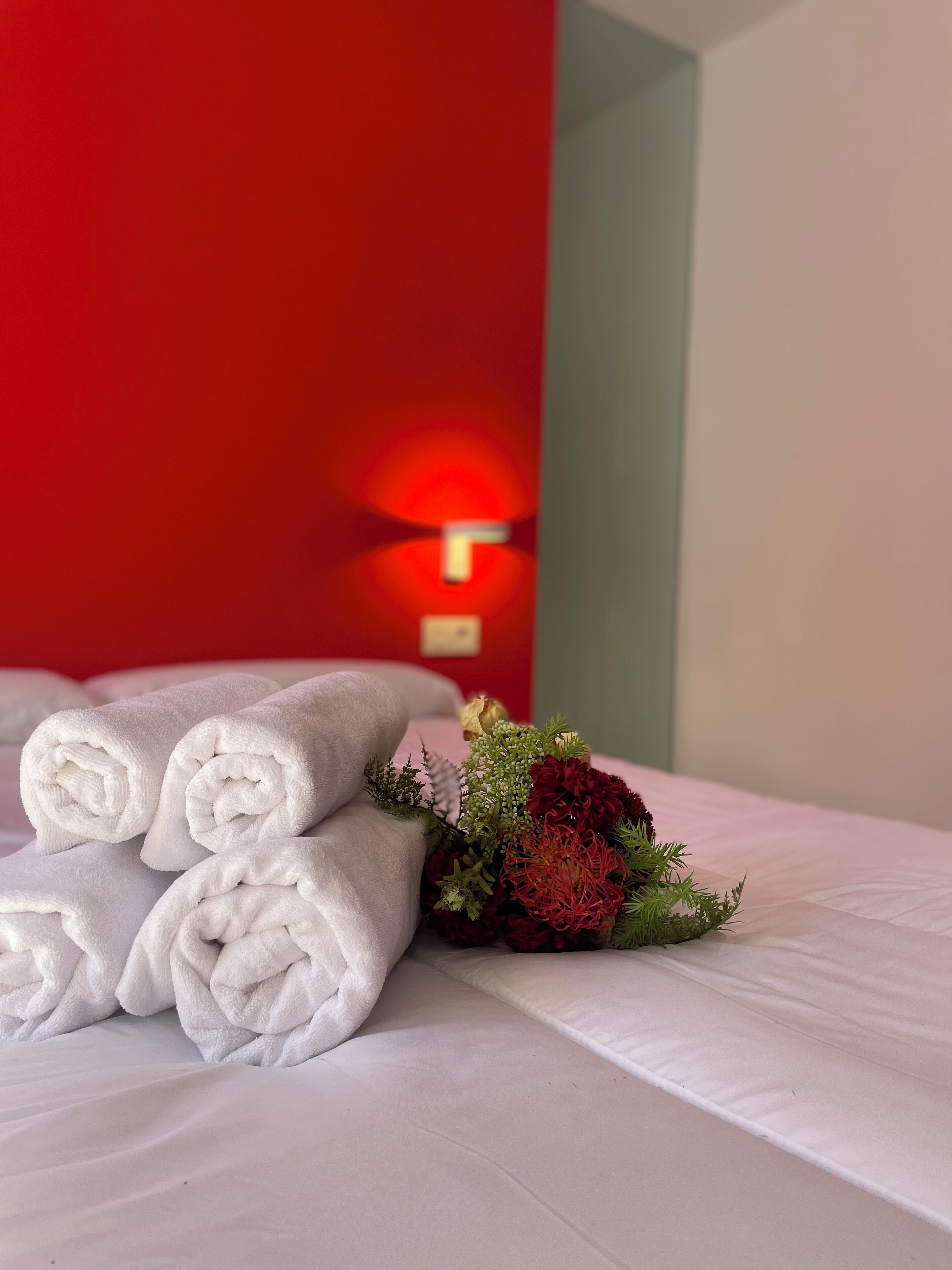 Una cama bien hecha con toallas blancas enrolladas y un arreglo floral.