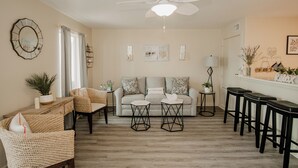 Ein Wohnzimmer mit einer Couch, zwei Sesseln, einem Couchtisch, einem Deckenventilator und einer Bar mit Hockern.