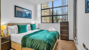 A modern hotel room with a large bed, a view of the city through a large window, and a cityscape painting on the wall. - Regent's Park Serviced Apartments (London)