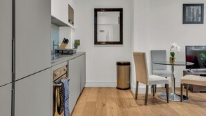 A modern kitchen with grey cabinets, a stainless steel sink, and a dining area with a glass table and chairs. - Regent's Park Serviced Apartments (London)