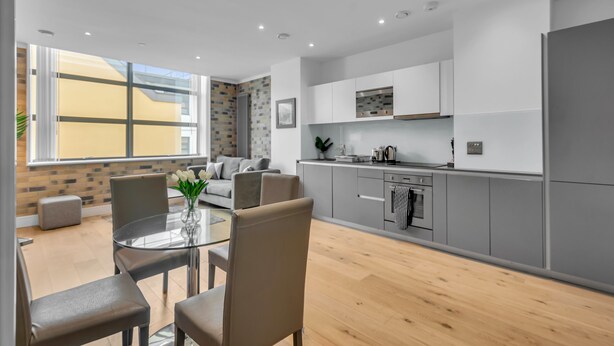 A modern kitchen with grey cabinets, a built-in oven, and a dining area with a glass table and chairs. - Regent's Park Serviced Apartments (London)