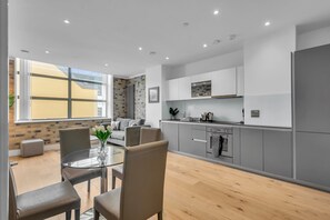 A modern kitchen with grey cabinets, a built-in oven, and a dining area with a glass table and chairs. - Regent's Park Serviced Apartments (London)