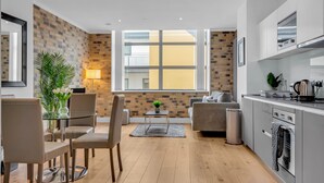 A modern living room with a glass dining table, comfortable seating, a coffee table, and a view of a cityscape through large windows. - Regent's Park Serviced Apartments (London)