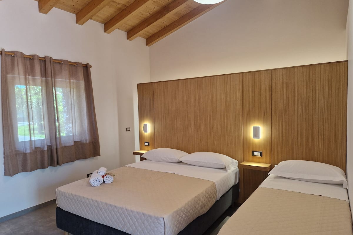 A hotel room with two beds, wooden headboards, bedside lamps, and a window with curtains.