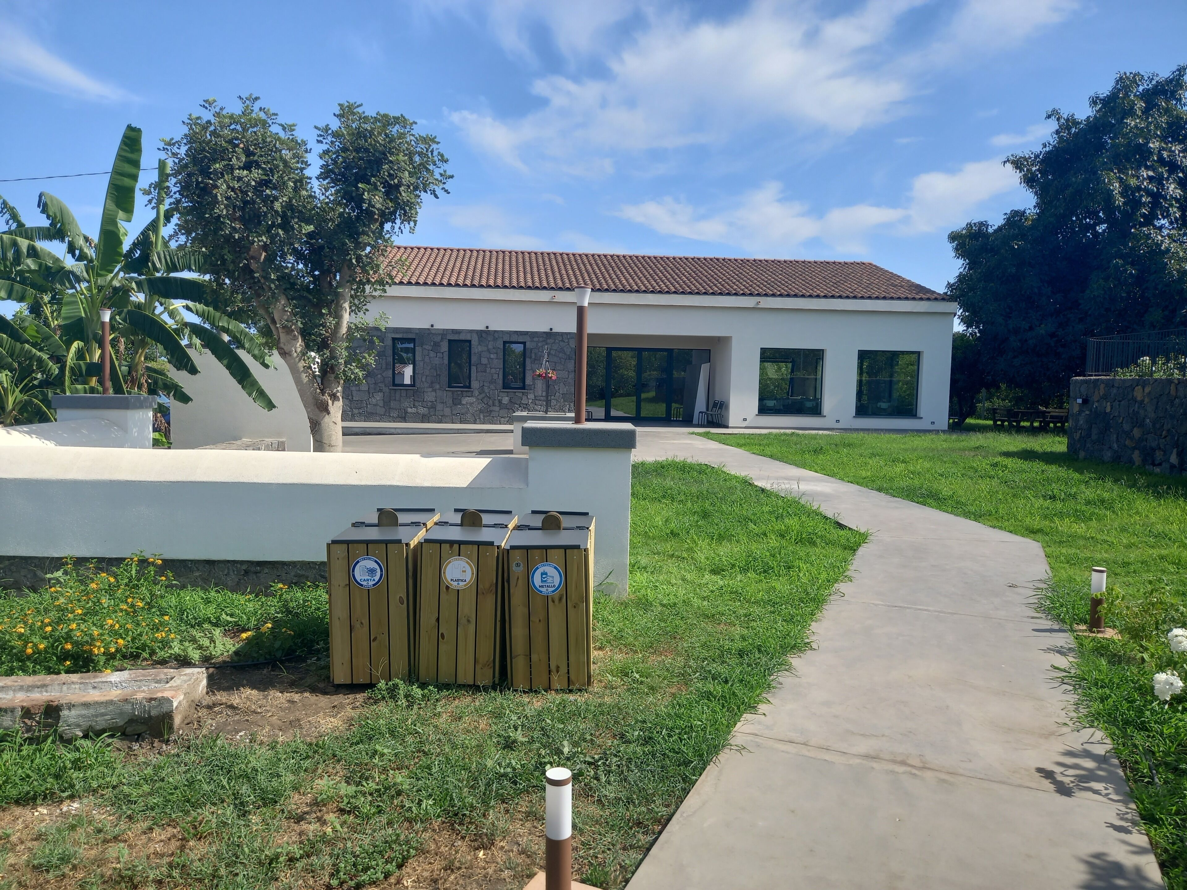 A modern building with a stone facade, a paved walkway, and wooden recycling bins.