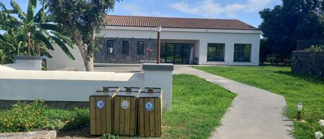 A modern building with a stone facade, a paved walkway, and wooden recycling bins.
