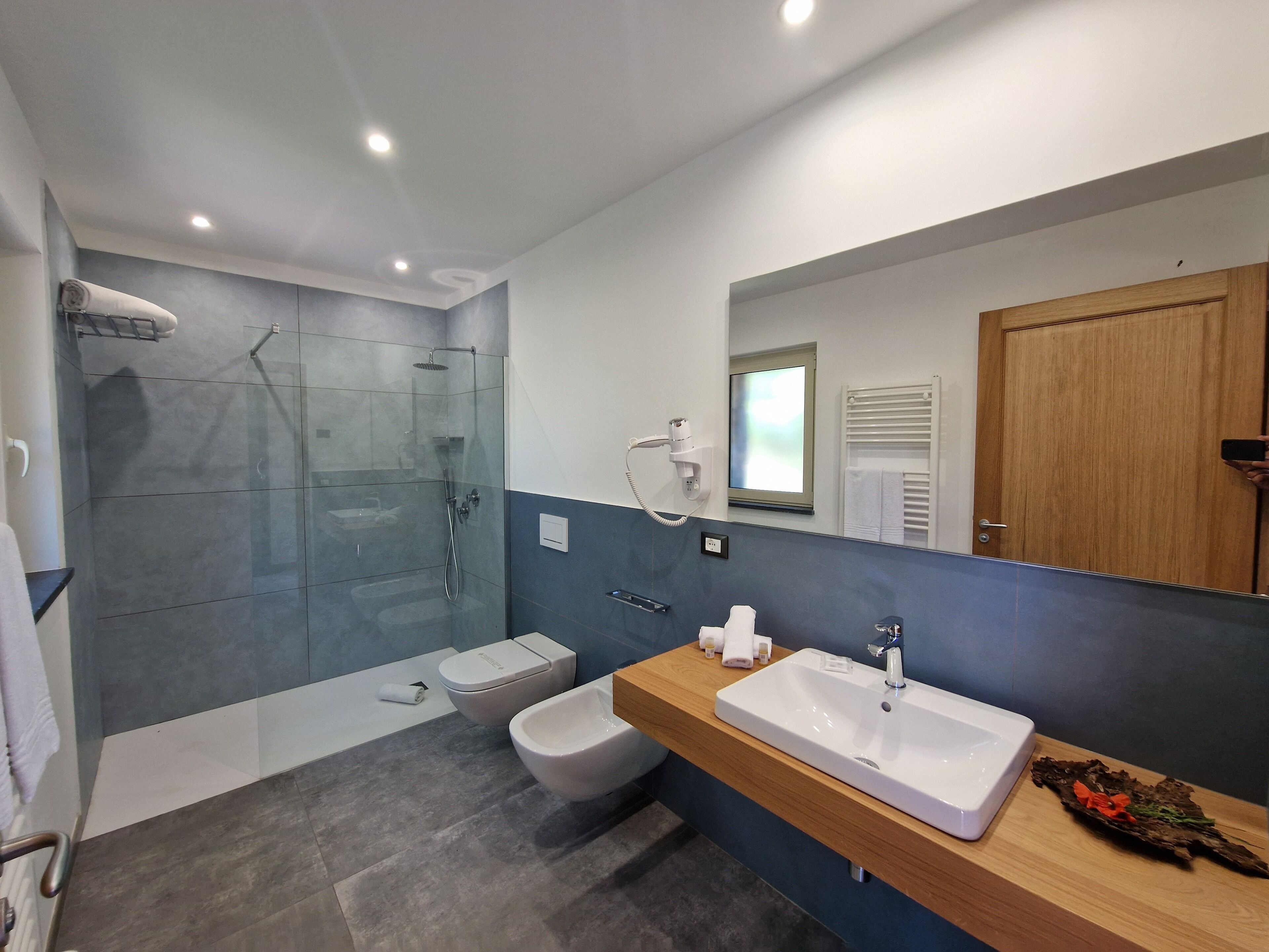 Een moderne badkamer met een douchecabine van glas, een witte wastafel en een houten badkamermeubel.