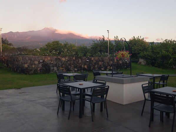 An outdoor patio with tables and chairs, a stone wall, and a view of mountains in the background. - Lumia Resort (Riposto)