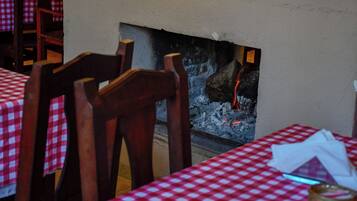 Interior de restaurante con manteles a cuadros, sillas de madera y una chimenea con leña a la vista.