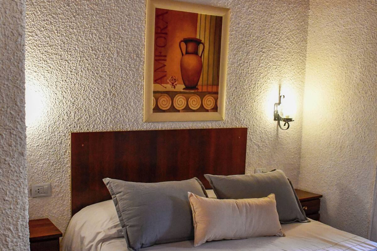 A bedroom with a wooden headboard, a painting above the bed, and a nightstand with a lamp.
