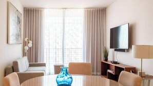 Une chambre d’hôtel avec une table à manger ronde, un vase bleu, un canapé, une télévision et une lampe.