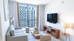 Une chambre d’hôtel moderne dotée d’une grande fenêtre, d’un téléviseur à écran plat, d’un canapé, d’une table basse et d’une petite table d’appoint.