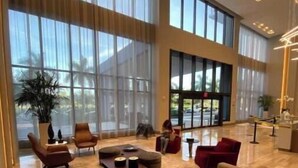 Un hallo espacioso con ventanas amplias, una zona de estar central con sofás y sillones, y un diseño moderno.