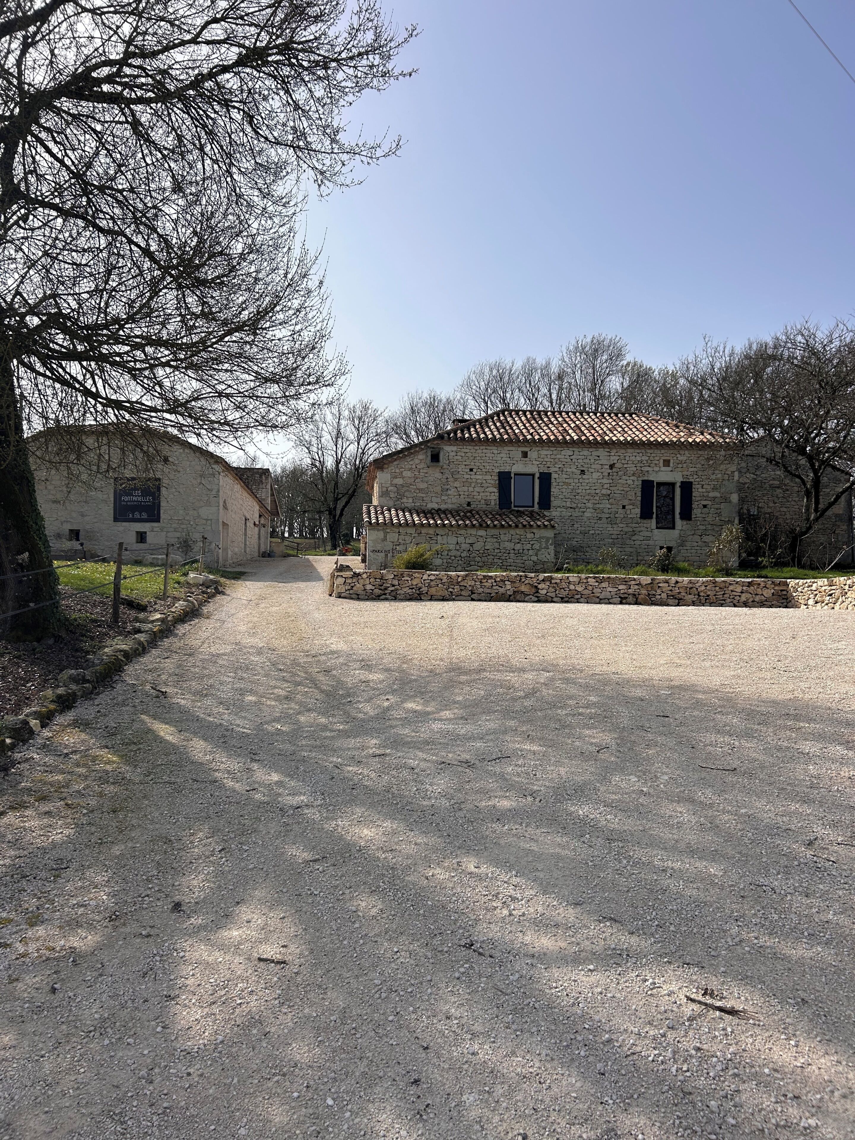 A stone building with a tiled roof, a gravel driveway, and a sign indicating 'Les Fortielles.'