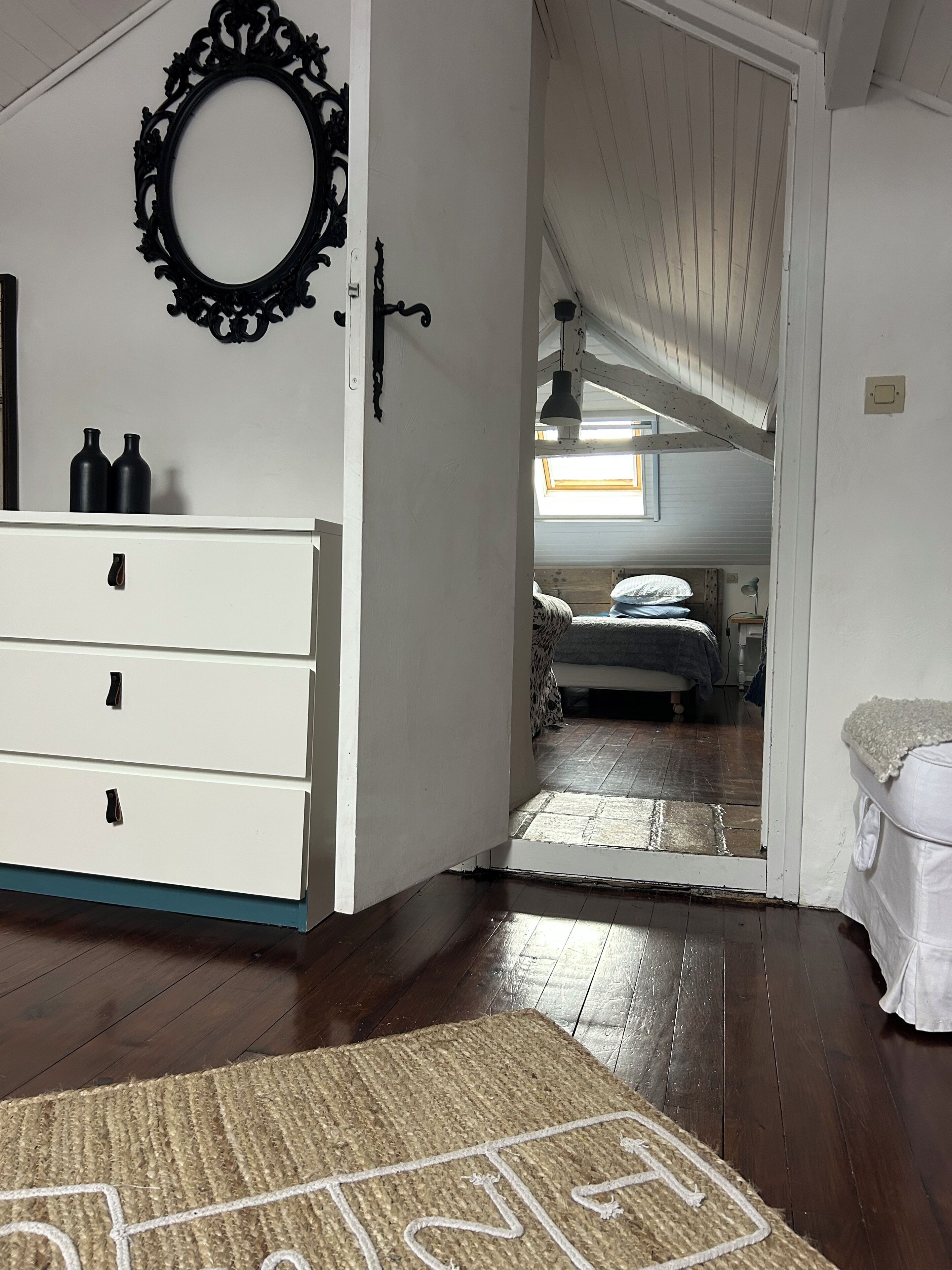 A room with a white dresser, a mirror, a door leading to another room, and a rug with a geometric pattern.