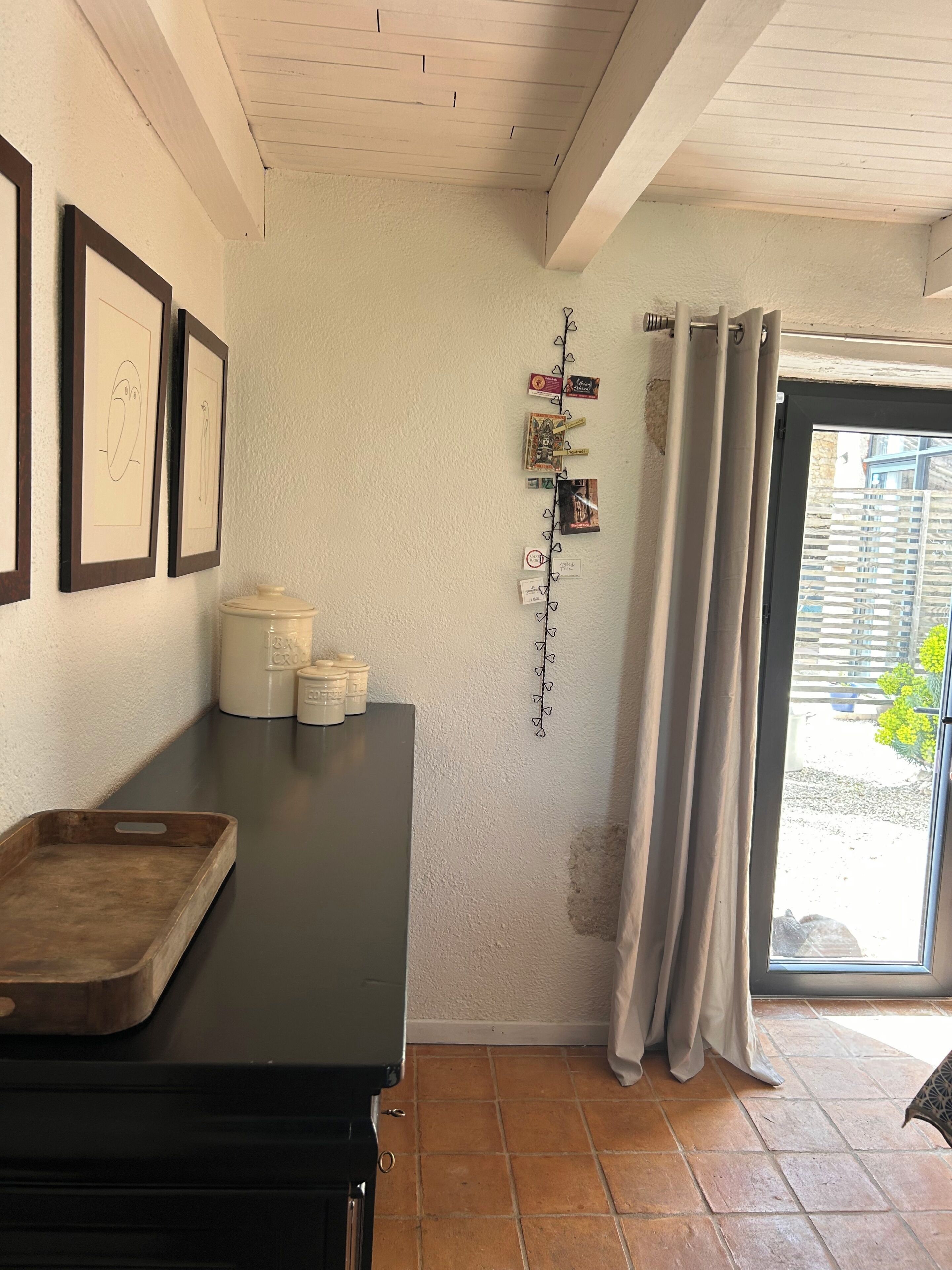 Une pièce avec une table en bois foncé, un mur blanc orné de dessins encadrés, une guirlande de décorations en forme de cœur et une fenêtre avec des rideaux.