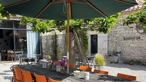 Une table en bois, des chaises orange et un parasol vert, le tout dans un cadre de jardin.