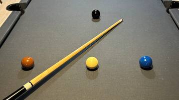 Une table de billard avec les billes disposées en forme de triangle, un queue de billard et une fenêtre en arrière-plan.