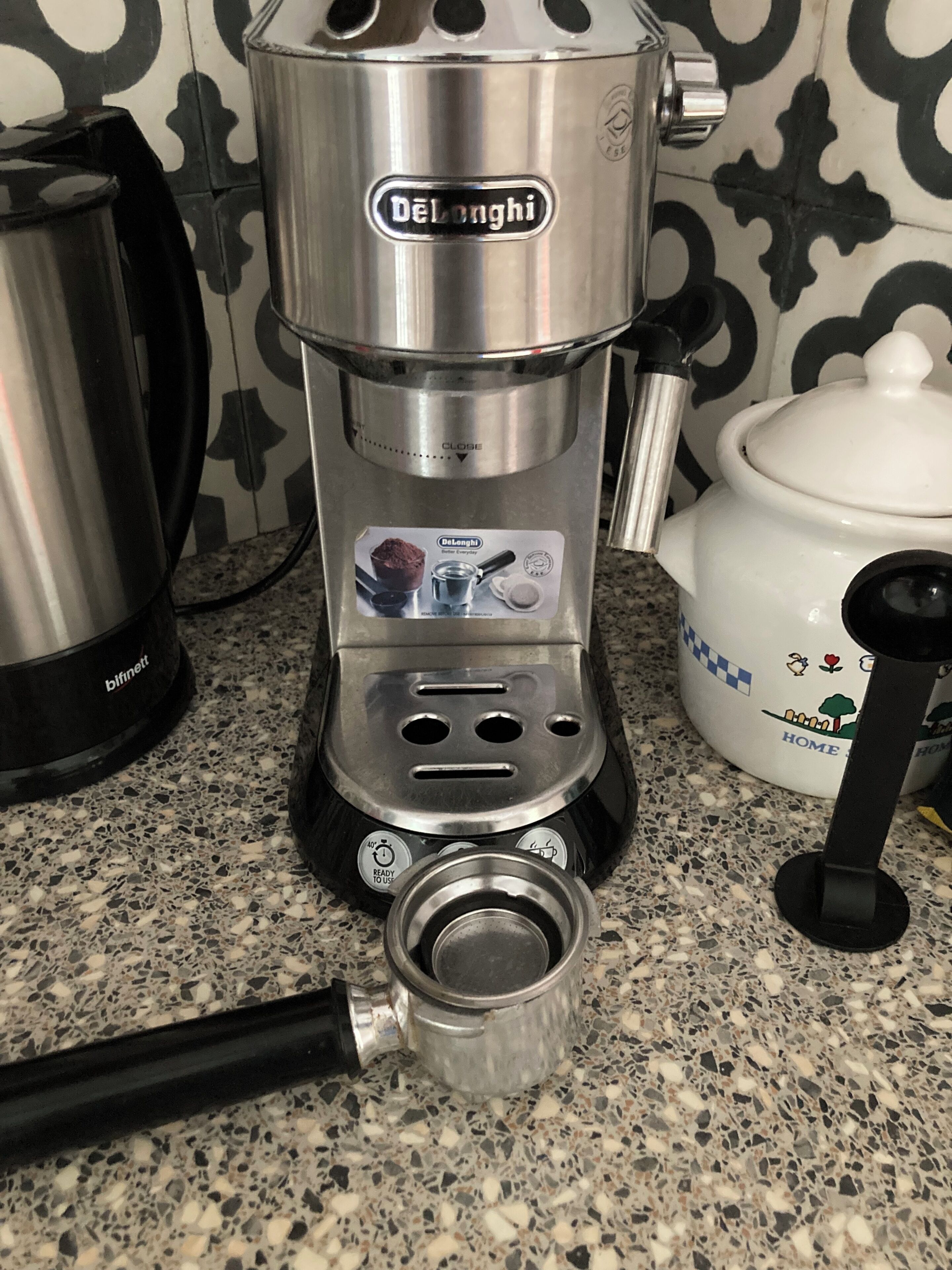 A De'Longhi coffee machine on a kitchen counter with a patterned backsplash.
