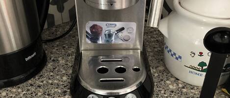 A De'Longhi coffee machine on a kitchen counter with a patterned backsplash.