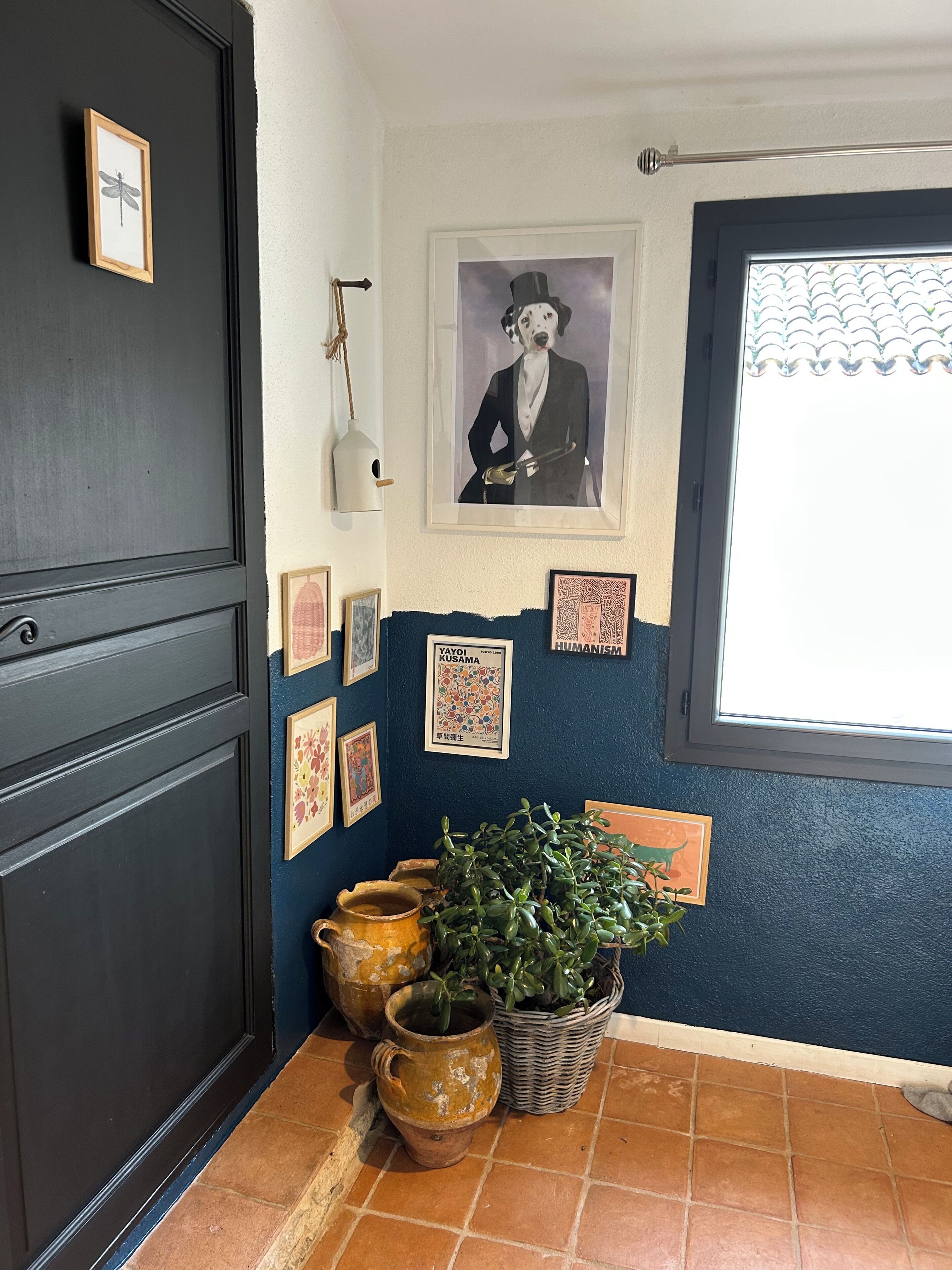 A room with a dark door, a window with a view, and various framed pictures on the wall.