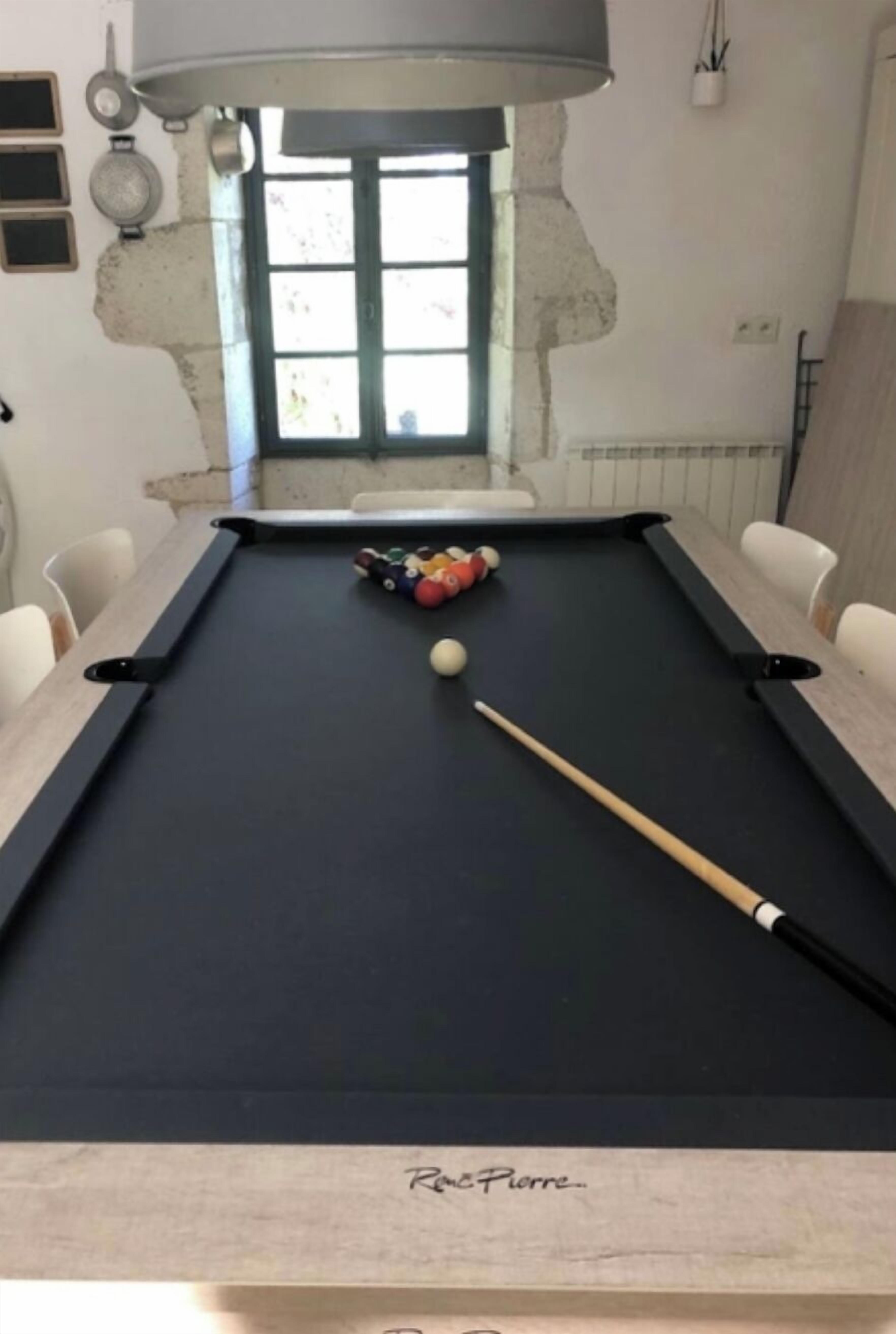 Una mesa de billar con taco, bolas de billar y una ventana al fondo.