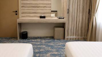 A hotel room with two beds, a desk, a mirror, a wardrobe, and a trash bin.