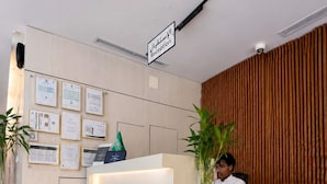 A reception desk with a sign indicating 'Reception' in Arabic, a man seated behind it, and framed documents on the wall. - Tallaq hotel (Madinah)